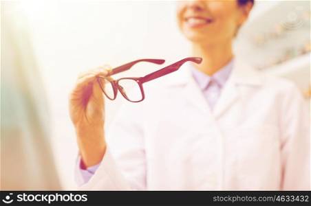 health care, people, eyesight and vision concept - close up of smiling woman optician holding glasses at optics store