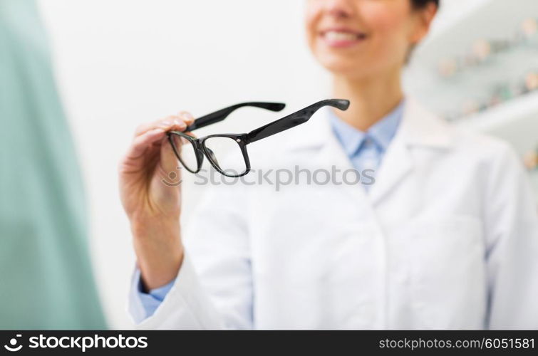 health care, people, eyesight and vision concept - close up of smiling woman optician holding glasses at optics store