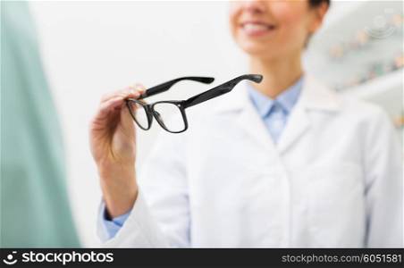 health care, people, eyesight and vision concept - close up of smiling woman optician holding glasses at optics store