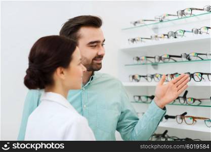 health care, people, eyesight and vision concept - female optician and man customer showing glasses at optics store