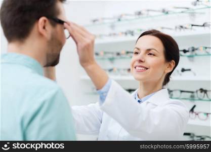 health care, people, eyesight and vision concept - female optician putting on glasses to man at optics store