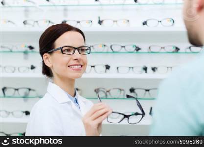 health care, people, eyesight and vision concept - female optician showing glasses to man at optics store