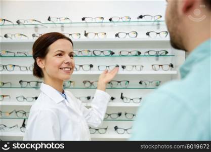 health care, people, eyesight and vision concept - female optician showing glasses to man at optics store