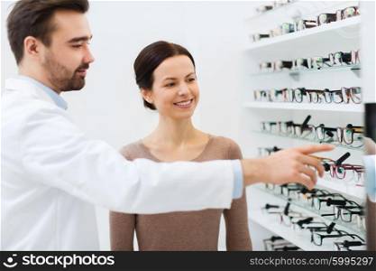 health care, people, eyesight and vision concept - happy woman choosing glasses with optician at optics store