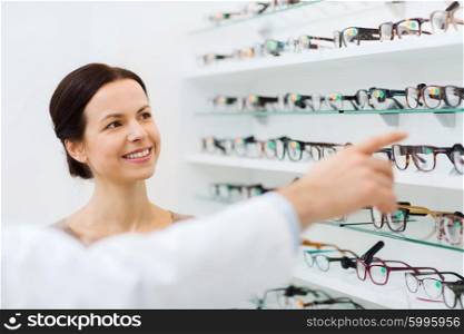 health care, people, eyesight and vision concept - happy woman choosing glasses with optician at optics store