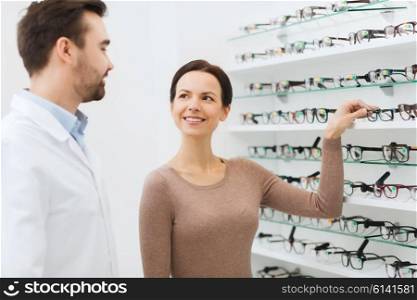 health care, people, eyesight and vision concept - happy woman choosing glasses and optician at optics store