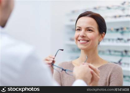 health care, people, eyesight and vision concept - happy woman taking glasses from optician at optics store