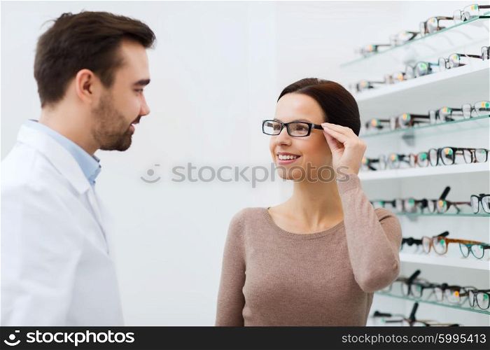 health care, people, eyesight and vision concept - happy woman with optician choosing glasses at optics store