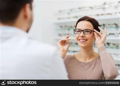 health care, people, eyesight and vision concept - happy woman with optician choosing glasses at optics store