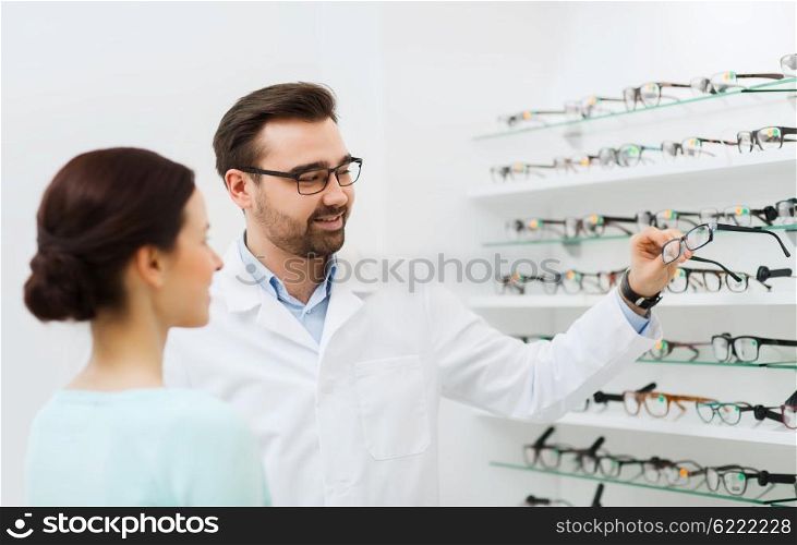 health care, people, eyesight and vision concept - optician choosing glasses for woman at optics store