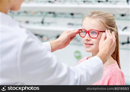 health care, people, eyesight and vision concept - optician putting glasses to little girl eyes at optics store