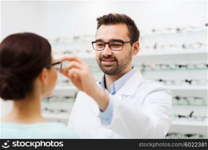 health care, people, eyesight and vision concept - optician putting glasses to woman at optics store
