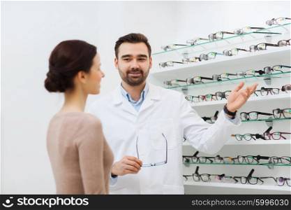 health care, people, eyesight and vision concept - optician showing glasses to woman at optics store