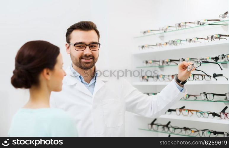 health care, people, eyesight and vision concept - optician showing glasses to woman at optics store