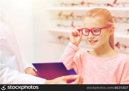 health care, people, eyesight and vision concept - optician with mirror helping little girl to choose glasses at optics store