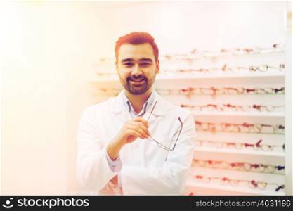 health care, people, eyesight and vision concept - smiling man optician holding glasses at optics store