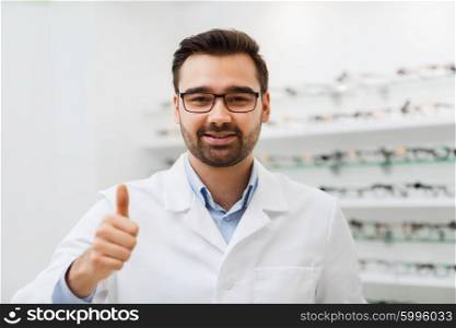 health care, people, eyesight and vision concept - smiling man optician in glasses and white coat showing thumbs up gesture at optics store