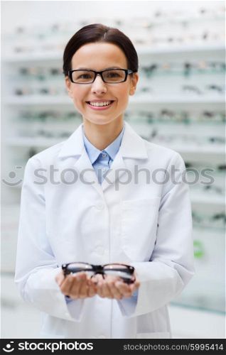 health care, people, eyesight and vision concept - smiling woman optician holding glasses at optics store