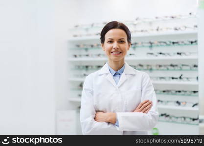 health care, people, eyesight and vision concept - smiling woman optician in white coat with glasses at optics store