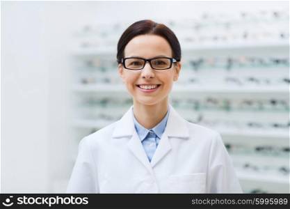 health care, people, eyesight and vision concept - smiling woman optician in glasses and white coat at optics store