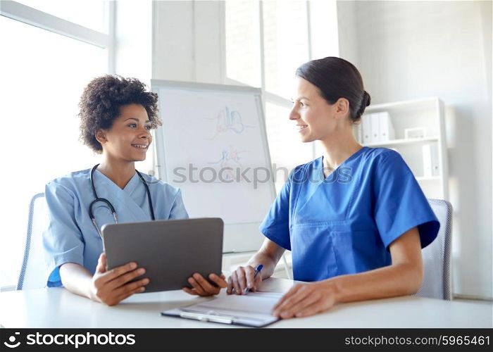 health care, people, technology and medicine concept -happy doctors with tablet pc computer and clipboard meeting and discussing something at hospital