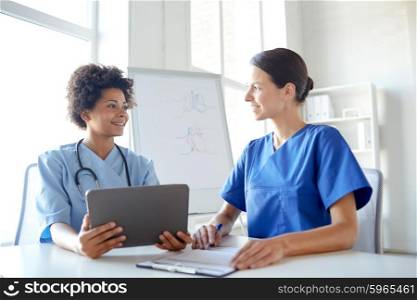 health care, people, technology and medicine concept -happy doctors with tablet pc computer and clipboard meeting and discussing something at hospital