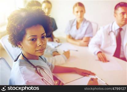 health care, profession, people and medicine concept - african american female doctor or nurse over group of medics meeting at hospital