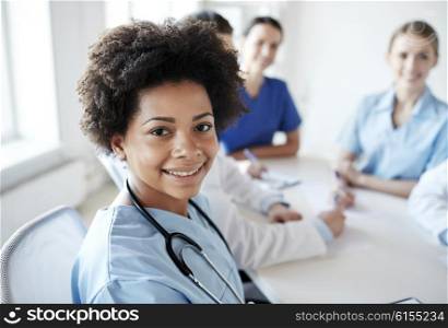 health care, profession, people and medicine concept - happy african american female doctor or nurse over group of medics meeting at hospital