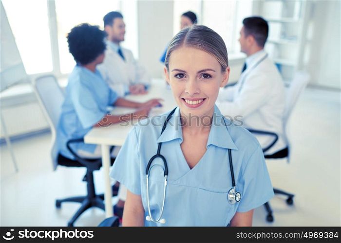 health care, profession, people and medicine concept - happy female doctor or nurse over group of medics meeting at hospital. happy doctor over group of medics at hospital
