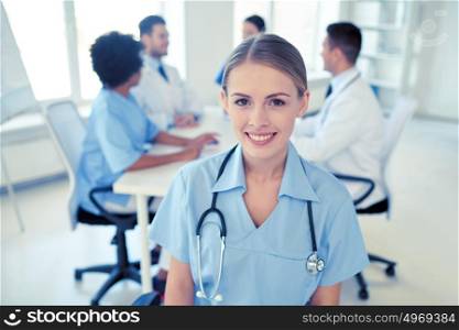health care, profession, people and medicine concept - happy female doctor or nurse over group of medics meeting at hospital. happy doctor over group of medics at hospital