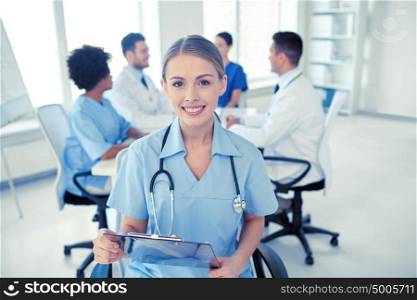 health care, profession, people and medicine concept - happy female doctor or nurse with clipboard over group of medics meeting at hospital. happy doctor with clipboard over group of medics