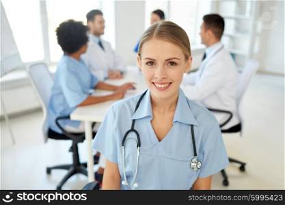 health care, profession, people and medicine concept - happy female doctor or nurse over group of medics meeting at hospital