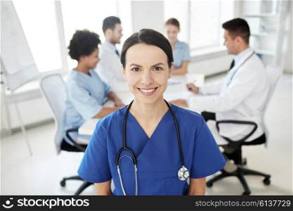 health care, profession, people and medicine concept - happy female doctor or nurse over group of medics meeting at hospital