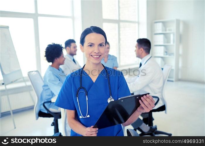 health care, profession, people and medicine concept - happy female doctor with clipboard over group of medics meeting at hospital. happy doctor with clipboard over group of medics