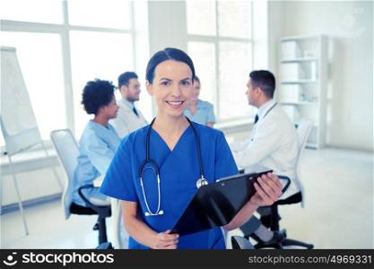 health care, profession, people and medicine concept - happy female doctor with clipboard over group of medics meeting at hospital. happy doctor with clipboard over group of medics
