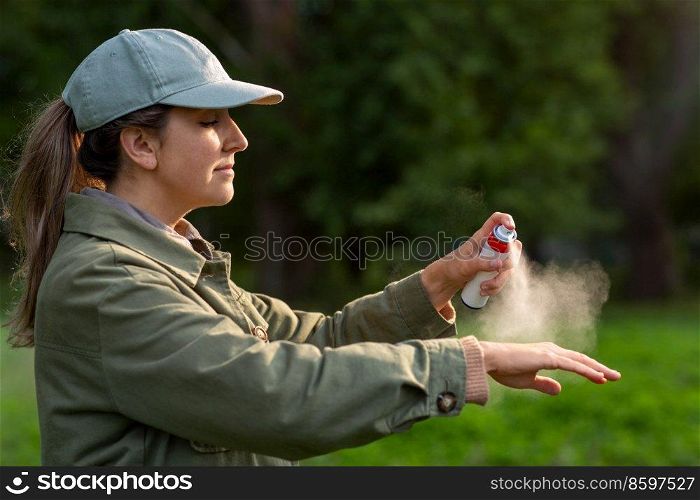health care, protection and people concept - woman spraying insect repellent or bug spray to her hand at park. woman spraying insect repellent to hand at park