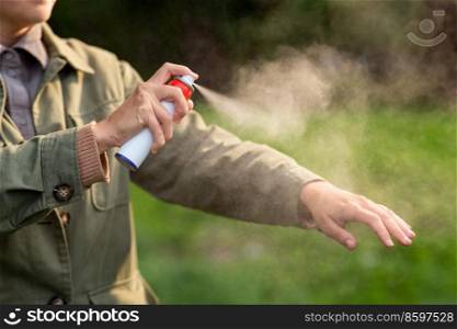health care, protection and people concept - woman spraying insect repellent or bug spray to her hand at park. woman spraying insect repellent to hand at park