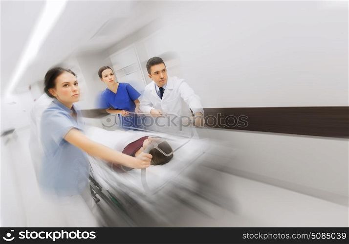 health care, reanimation and medicine concept - group of medics or doctors carrying unconscious woman patient on hospital gurney to emergency (motion blur effect). medics and patient on hospital gurney at emergency. medics and patient on hospital gurney at emergency