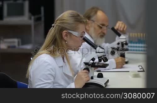 Health care researchers working in life science laboratory. Young scientist and her post doctoral supervisor looking at microscope slides in research lab and talking. Scientific team looking through microscope in laboratory, researching, discussing