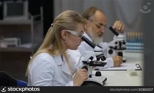Health care researchers working in life science laboratory. Young scientist and her post doctoral supervisor looking at microscope slides in research lab and talking. Scientific team looking through microscope in laboratory, researching, discussing
