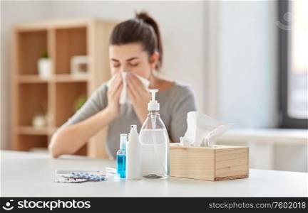 health care, virus and people concept - medicines and sanitizers on table over sick woman blowing nose to paper wipe at home. medicines and sick woman blowing nose to wipe