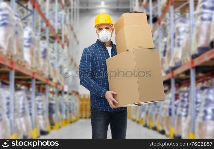 health care, work and pandemic concept - male worker in safety helmet and face protective mask or respirator with boxes over warehouse background. worker in respirator mask with boxes at warehouse