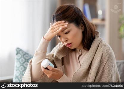 health, cold and people concept - sad sick young asian woman having headache with painkiller medicine at home. sick asian woman with painkiller medicine at home