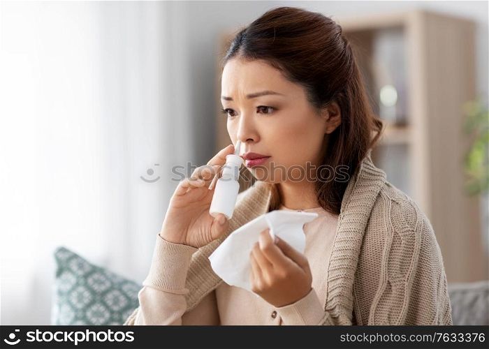 health, cold and people concept - sad sick young asian woman in blanket using nasal spray medicine and paper tissue at home. sick asian woman with nasal spray medicine at home