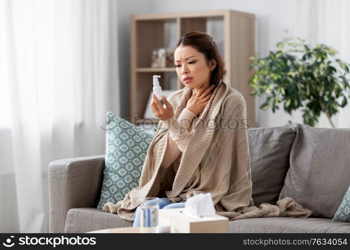 health, cold and people concept - sad sick young asian woman in blanket with oral spray medicine at home. sick asian woman with oral spray medicine at home