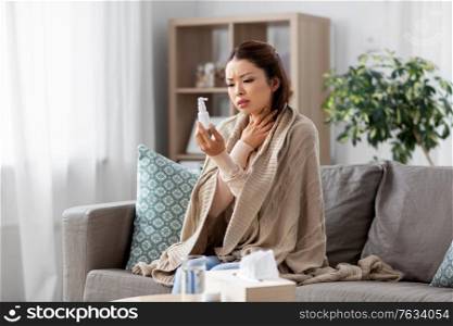 health, cold and people concept - sad sick young asian woman in blanket with oral spray medicine at home. sick asian woman with oral spray medicine at home