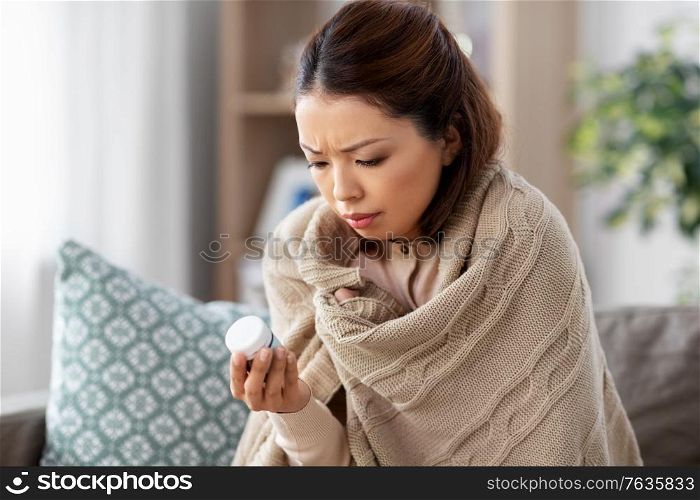 health, cold and people concept - sad sick young asian woman in blanket with medicine at home. sick asian woman with medicine at home