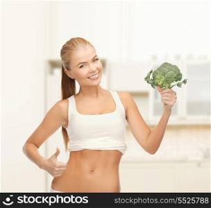 health, diet and food concept - beautiful woman pointing at her abs and holding broccoli