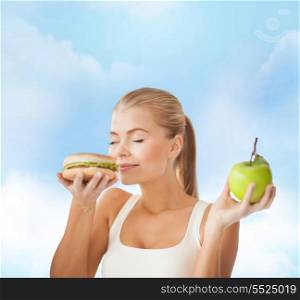 health, diet and food concept - happy woman smelling hamburger and holding apple