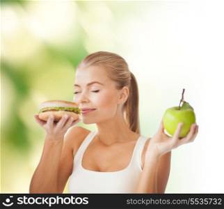 health, diet and food concept - healthy woman smelling hamburger and holding apple